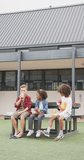 Vertical video of three diverse schoolchildren eating packed lunches, talking outdoors, copy space. Education, childhood, inclusivity, school and learning concept.
