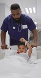 Vertical video of african american male doctor walking with child patient at hospital. Medicine, healthcare, lifestyle and hospital concept.