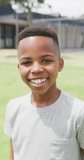 Vertical video portrait of happy african american schoolboy smiling in schoolyard, copy space. Education, childhood, inclusivity, school and learning concept.
