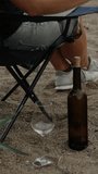 A young woman on the beach by the sea drinks wine straight from the bottle. Vertical video Social Media