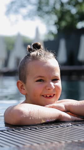 Young boy swiming at the pool. Child in the pool looking at the camera and smiling. Portrait of 7-8 years kid on summer vacation outdoor pursuit. Vertical video format