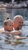 Father and son together in pool. Dad teaches his son to swim. The child swims in the pool. Vertical video format