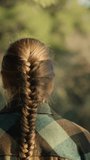 A young woman with long hair and a scythe walks through the forest at sunset. Vertical video Social Media