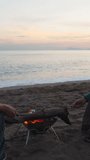 Romantic date by the sea at sunset, A young couple frying marshmallows by the campfire. Vertical video Social Media