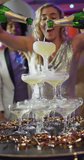 Vertical video of happy caucasian woman pouring a champagne fountain into glasses at nightclub. Fun, drinking, going out and party concept.