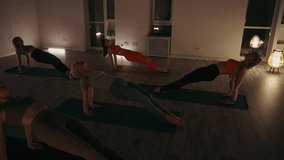 Group of individuals is engaged in a yoga session, focusing on their core and balance as they execute the reverse plank pose. The dimly lit room creates a tranquil atmosphere for the evening workout - Powered by Shutterstock - Get 15% off with code: PIKWIZARD15