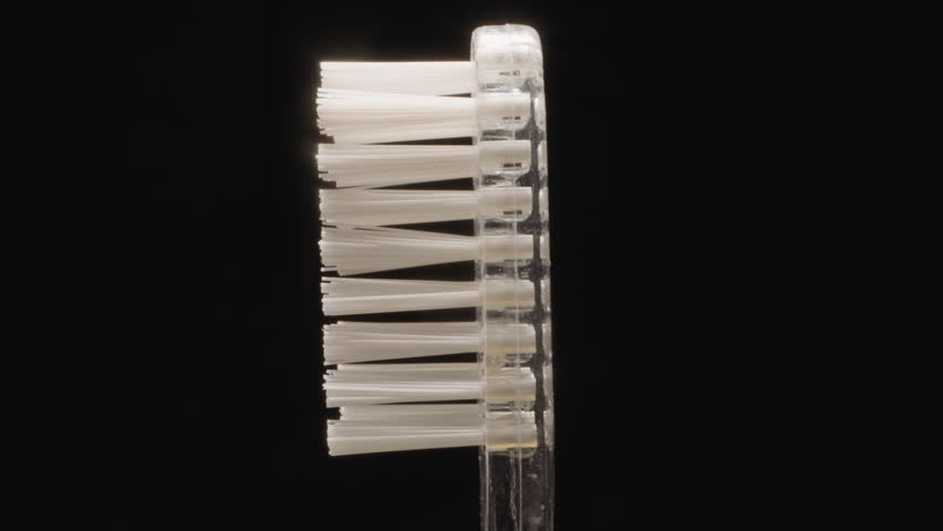 Transparent plastic toothbrush with hard white bristles turning on black background. Small brush designed for professional oral hygiene macro