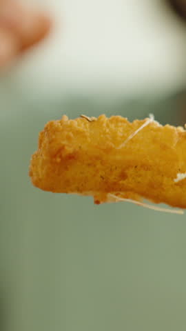 The young woman breaks a cheese stick and the cheese stretches out of it, close-up, slow motion. Vertical video Social Media