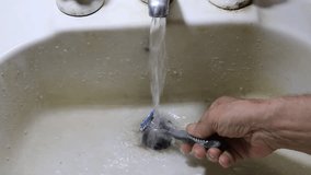 Man washes his razor after shaving in old white bathroom, under running water to clean shaving foam for daily routine personal care