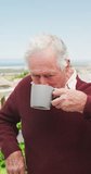Vertical video of happy caucasian senior man drinking coffee on balcony. Active retirement and lifestyle concept.