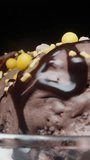 Balls of chocolate ice cream and sugar sprinkles rotate and I pour them with chocolate, close-up Vertical video Social Media