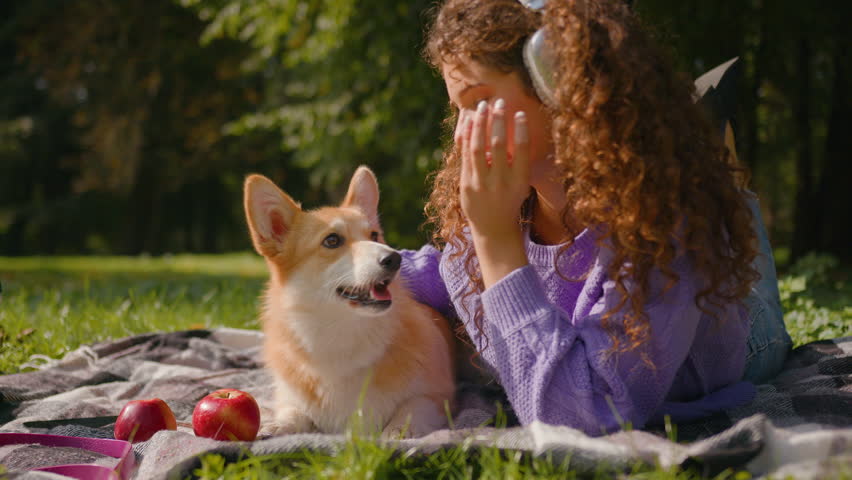 Happy Caucasian woman girl listen music headphones in park city weekend outdoors playing lovely dog welsh corgi breed sweet puppy on grass cute pup licking hand doggy owner pet friendly cuddling smile Royalty-Free Stock Footage #3457614919