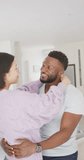 Vertical video of happy diverse couple dancing in living room. Spending quality time at home concept.