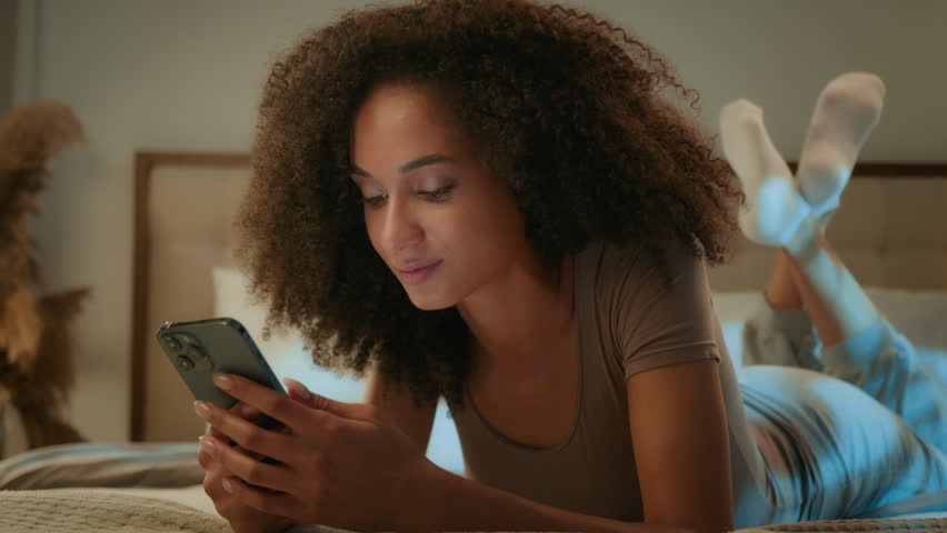 Surprised shocked young African American woman evening night scrolling mobile phone on bed in home bedroom amazed excited girl browsing smartphone win online good message wonder shock wow excitement Royalty-Free Stock Footage #3457630279