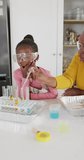 Vertical video of excited african american granddaughter and grandmother doing chemistry, copy space. Science, education, learning, family and domestic life.