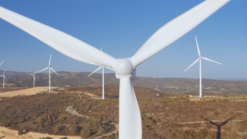 Blade wind turbine rotating close-up. Wind farm on dry yellow field, blue sky in background. Alternative energy technology. Renewable energy source. Nature environment. Beautiful summer landscape.