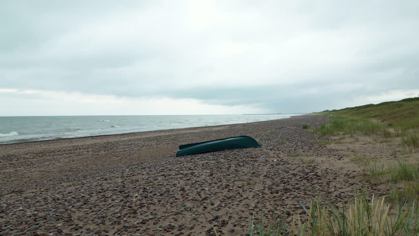 A green canoe rests on beach sand with ocean horizon in sight