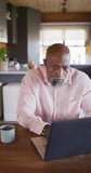 Vertical video of senior african american man spending time in log cabin and using laptop. Free time, domestic life and nature concept.