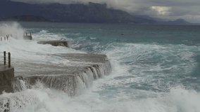 Sea waves break on the stone pier. Slow motion