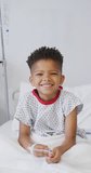 Vertical video of portrait of african american boy smiling at hospital. Medicine, healthcare, lifestyle and hospital concept.
