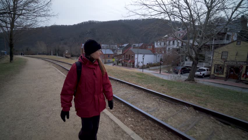 Mature woman walking along a railroad track and looking at the historic town of Harpers Ferry National Park in Harpers Ferry, West Virginia.