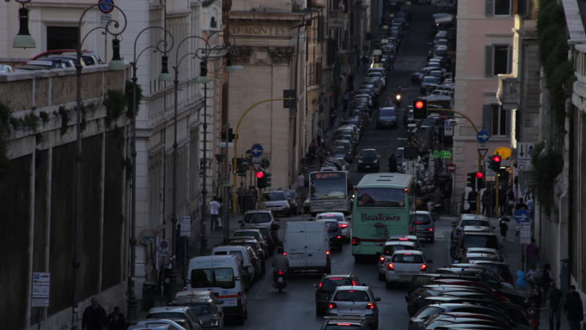 Cars and buses driving down a narrow street at intersection with cars parked