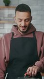 Vertical video. Man stirring soup with spoon and tasting. Happy male enjoying food taste indoors. Smiling chef cooking meal at domestic kitchen