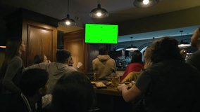 Group of multi ethnic friends sit in sports pub and watch live match broadcast on TV with Green Screen Chromakey. Fans gathered to cheer and support team playing in tournament. Crowd celebrate. - Powered by Shutterstock - Get 15% off with code: PIKWIZARD15