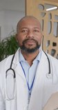Vertical video of portrait of african american male doctor smiling at hospital. Medicine, healthcare, lifestyle and hospital concept.