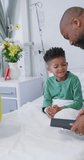 Vertical video of african american male doctor and child patient using tablet at hospital. Medicine, healthcare, lifestyle and hospital concept.