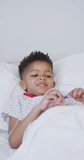 Vertical video of african american boy laying in bed at hospital. Medicine, healthcare, lifestyle and hospital concept.