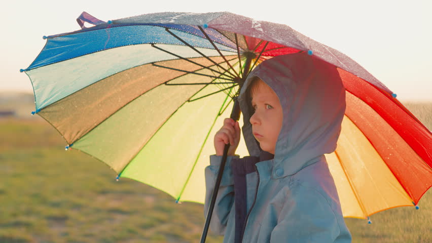 Child stands alone in field on rainy day. Each droplet on umbrella serves as reminder of unsettled emotions swirling in head. Overshadowed by relentless rain Royalty-Free Stock Footage #3457868057