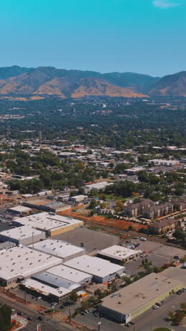 Picturesque green panorama of Salt Lake City on sunny hot day. Mountainous skyline at backdrop. Aerial view. Vertical video.