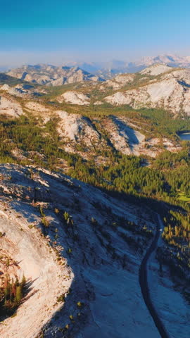 Grey rocks overgrown with pine trees on sunny daytime. Beautiful azure lakes locating among the gorgeous rocks of Yosemite National Park, California, USA. Aerial view. Vertical video.