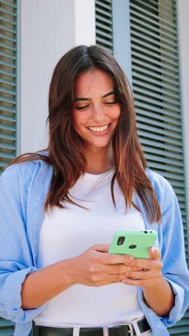 Vertical portrait of a smiling young woman using mobile phone app , texting, playing game, shopping online, ordering delivery. Happy millennial teen girl sharing social media holding smartphone. High