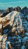 Aerial around view of amazing rocky mountains in snow at sunrise, Dolomites, Italy. Vertical video