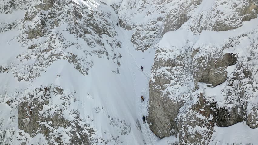 A team of climbers connected by a climbing rope are ascending a snow-covered incline. They are equipped with helmets and safety gear. Royalty-Free Stock Footage #3457947935