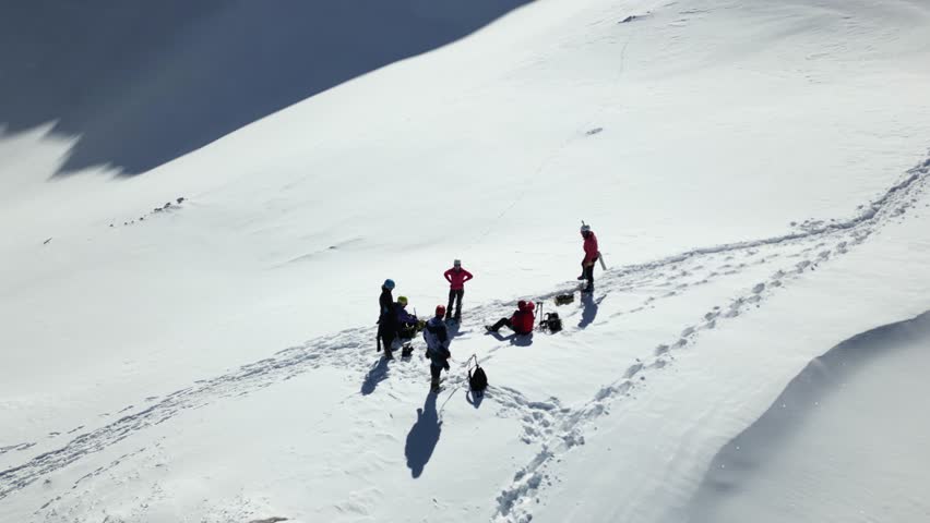 Aerial view of a group of alpinists walking on snow-covered mountain. They wear helmets and safety equipment. Mountaineering, climbing, alpinism concept. Royalty-Free Stock Footage #3457955001