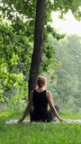 Yoga meditation practice in nature. Back view of unrecognizable woman practicing yoga in summer forest outdoors. Meditation pose, lotus position, raising hands up, doing stretching exercise. Vertical 