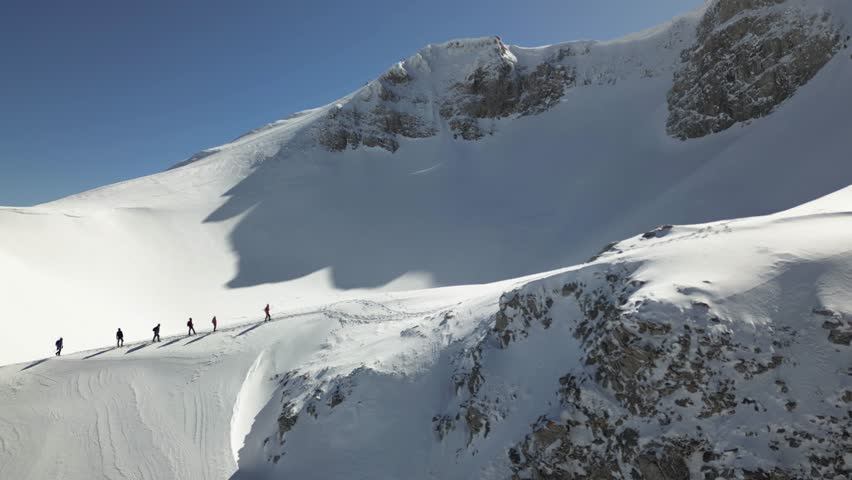 Aerial view of a group of alpinists walking on snow-covered mountain. They wear helmets and safety equipment. Mountaineering, climbing, alpinism concept. Royalty-Free Stock Footage #3457956565