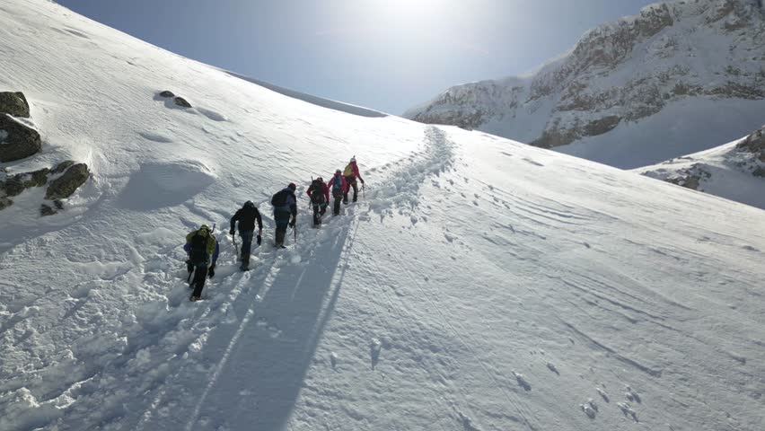 Aerial view of a group of alpinists walking on snow-covered mountain. They wear helmets and safety equipment. Mountaineering, climbing, alpinism concept. Royalty-Free Stock Footage #3457958721