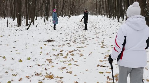 Back of woman walk with sticks near woman and girl on winter road in park, slow motion.