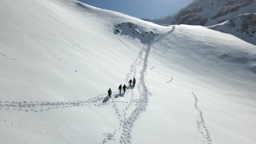 Aerial view of a group of alpinists walking on snow-covered mountain. They wear helmets and safety equipment. Mountaineering, climbing, alpinism concept. Royalty-Free Stock Footage #3457961557