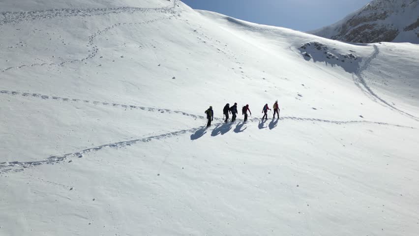 Aerial view of a group of alpinists walking on snow-covered mountain. They wear helmets and safety equipment. Mountaineering, climbing, alpinism concept. Royalty-Free Stock Footage #3457962945