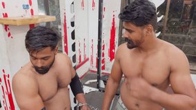 Two fit men posing confidently at a gym with exercise equipment in the background with hand cuff both prisoner hands motivation video for gym Asia india