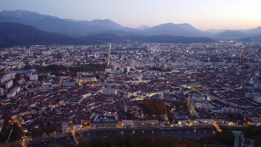 Drone shot of Grenoble, France from a high point with a view of the city in the evening. Cars and city lights can be seen in the mist of a cold evening in October. 