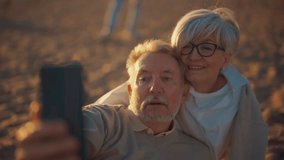 Romantic senior couple makes selfie on sea beach talking resting together. Man hugging woman taking photos on smartphone at sunset in evening, spending time. Relationships, lifelong romance marriage. - Powered by Shutterstock - Get 15% off with code: PIKWIZARD15
