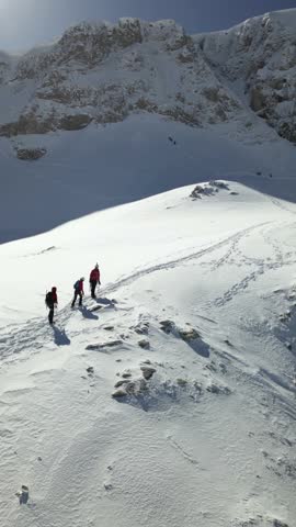 Aerial view of a group of alpinists walking on snow-covered mountain. They wear helmets and safety equipment. Mountaineering, climbing, alpinism concept. Royalty-Free Stock Footage #3458100499