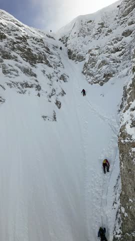 A team of climbers connected by a climbing rope are ascending a snow-covered incline. They are equipped with helmets and safety gear. Royalty-Free Stock Footage #3458108955
