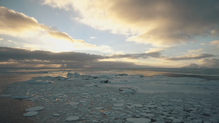 Polar sunset Dawn over Antarctic coast. Ocean covered ice. Top above aerial view. Antarctica snow mountain. Sky sunrise Antarctica winter. Open water. Beautiful sky landscape. Top Drone Flight